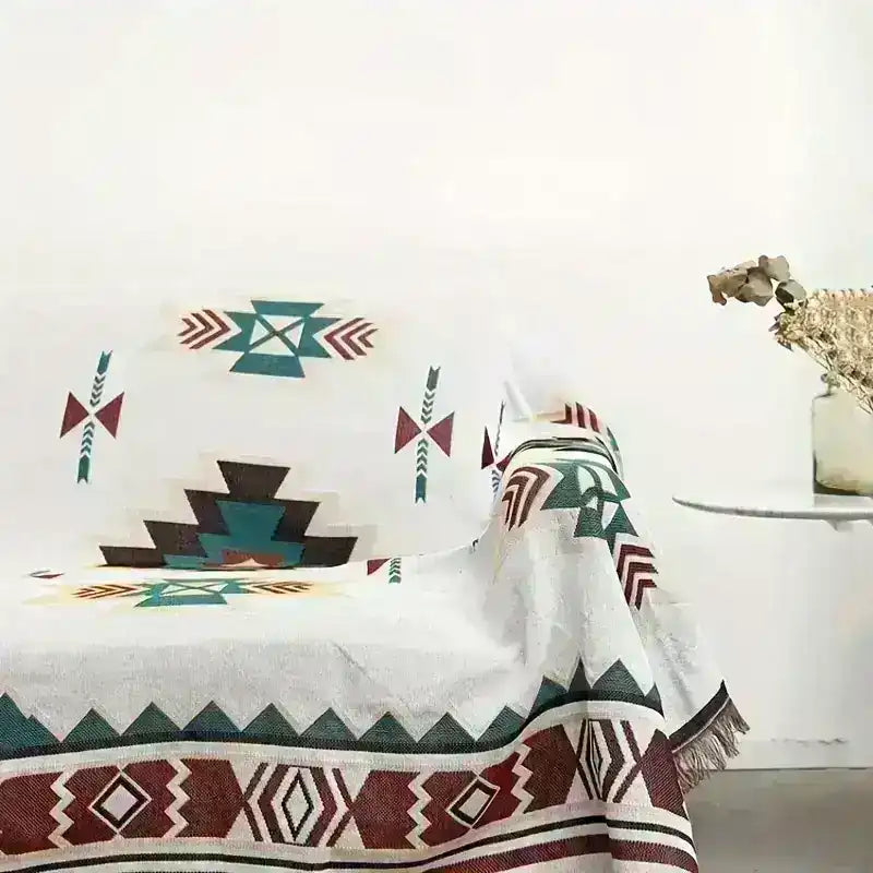 Sofa draped with geometric patterned Middle Eastern throw blanket next to a table with dried flowers.