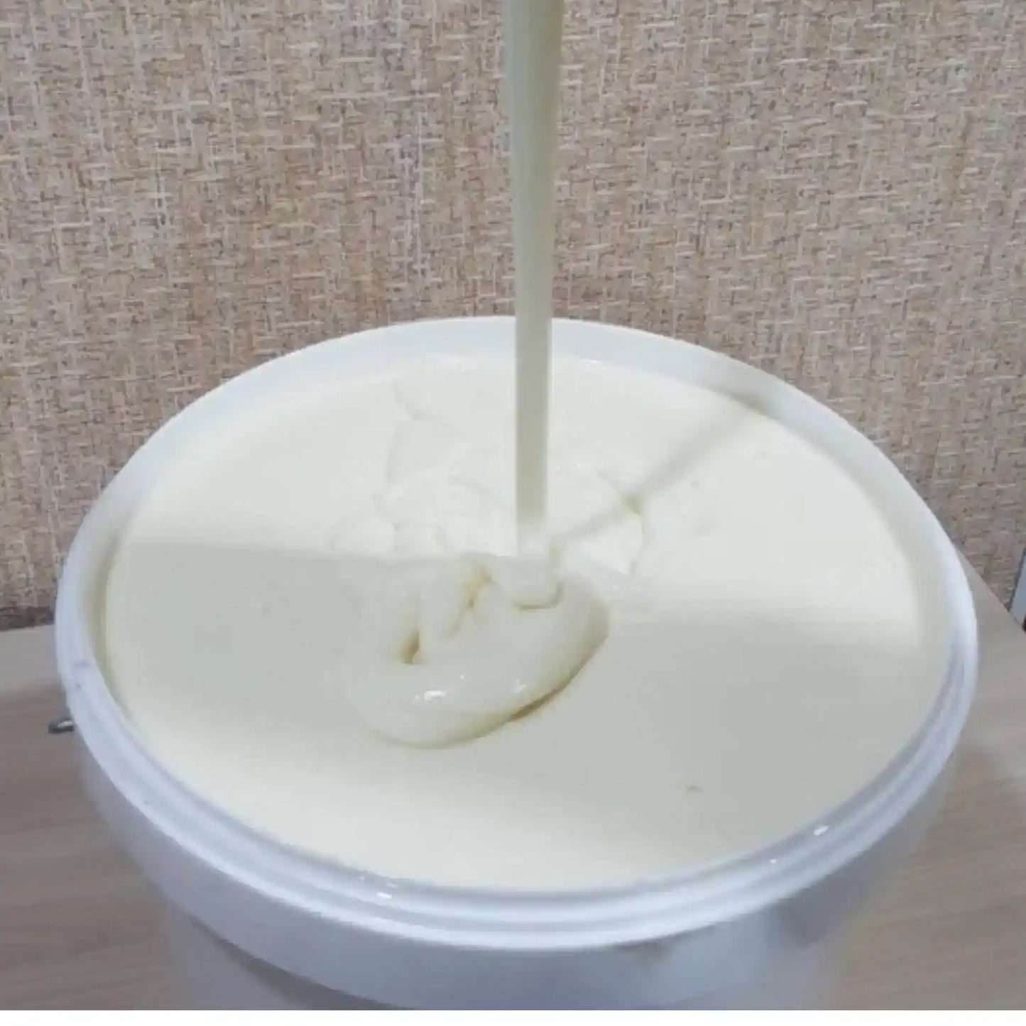 Creamy tahini paste being poured into a white tub, Middle Eastern food ingredient