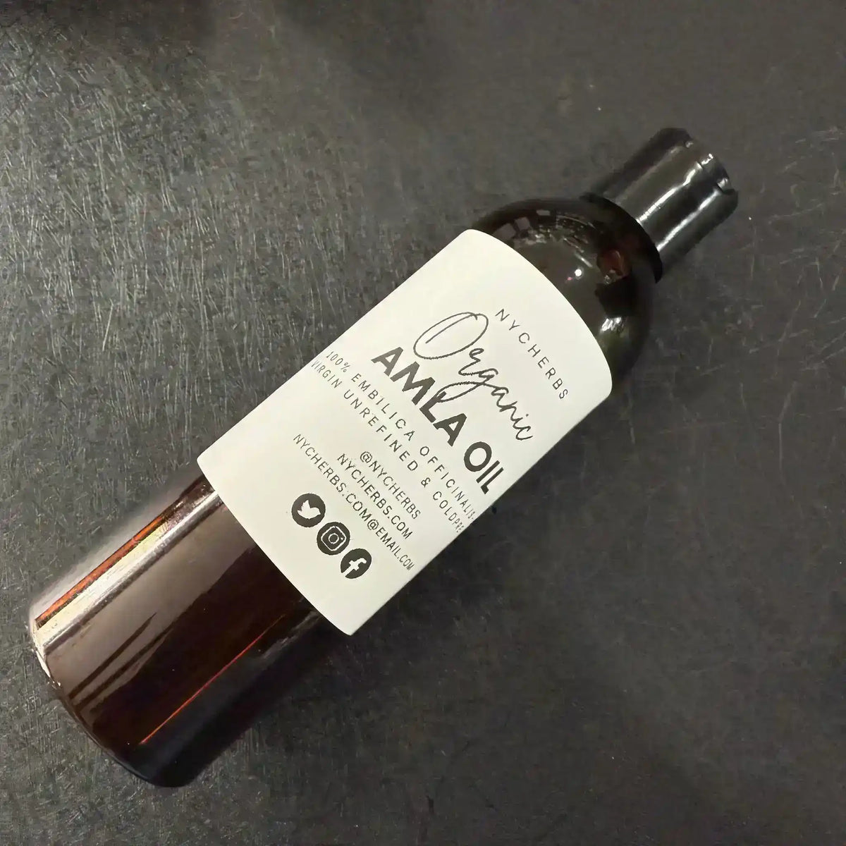 Brown bottle of organic amla oil with white label on a black surface