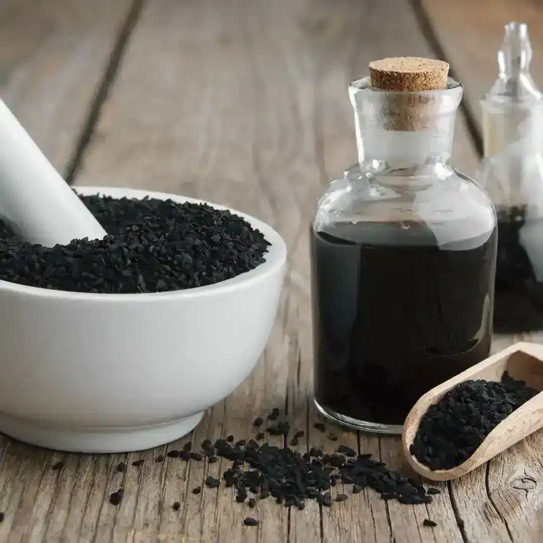 Black seed oil in glass bottle with whole black cumin seeds and mortar on wooden table