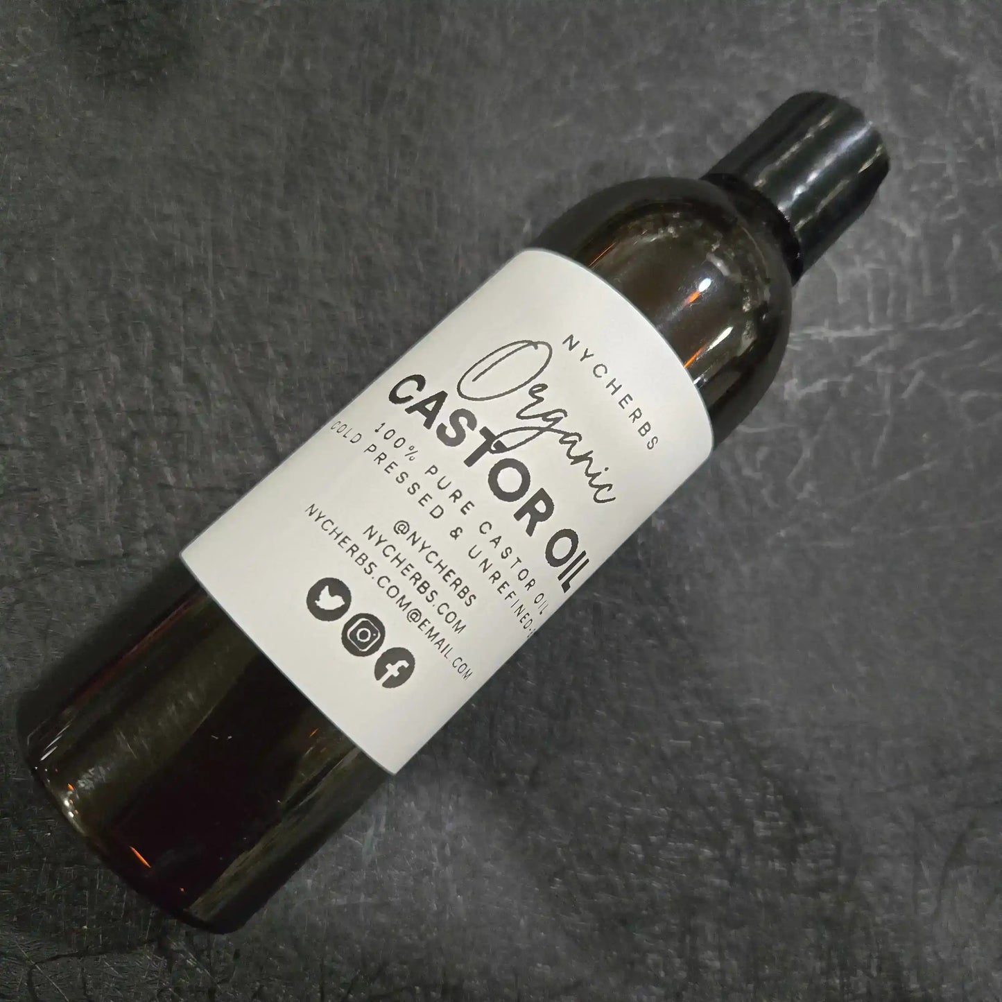 Bottle of organic castor oil with white label on textured black background