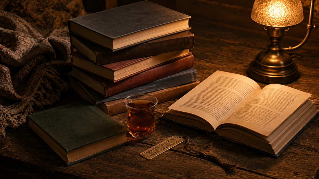 Stack of hardback books with plain spines and one lying open beside a glass of tea and a brass bookmark on aged wood