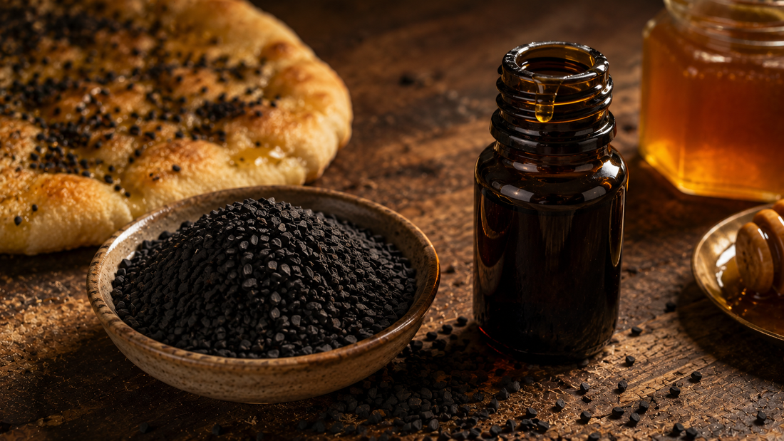 Ceramic bowl of matte black seeds scattered on aged wood beside an open amber bottle of cold-pressed black seed oil, honey and seeded flatbread