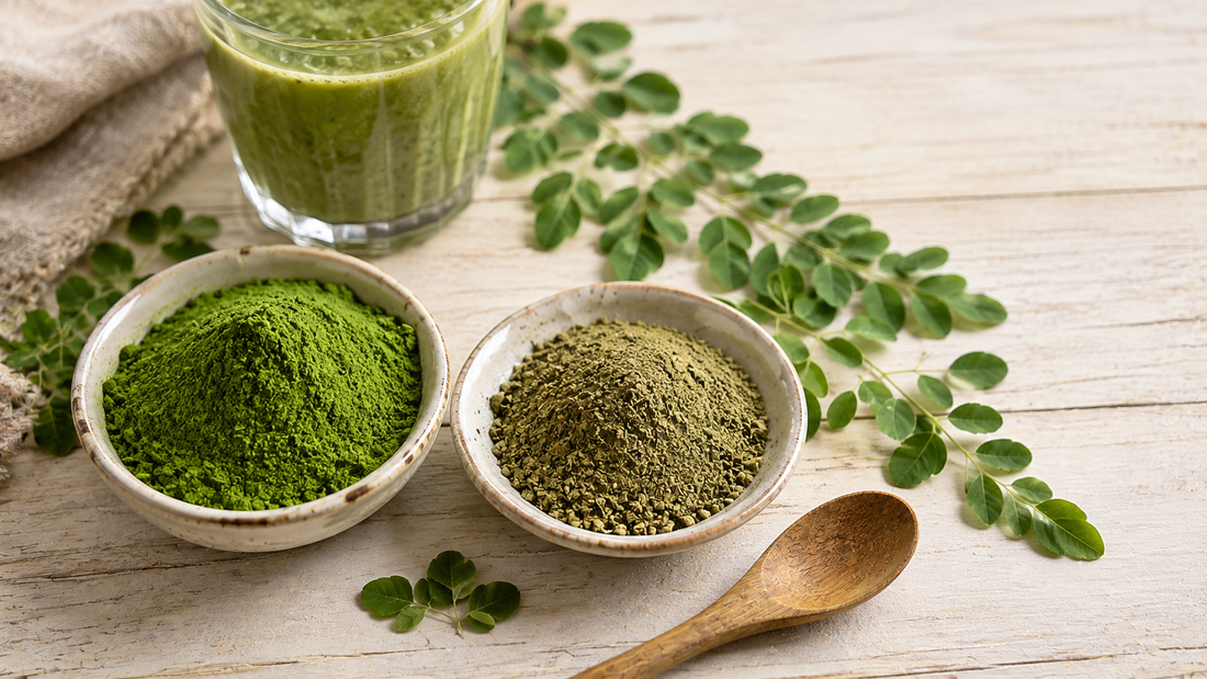 Bowl of vivid green moringa powder beside a duller olive-green sample with fresh moringa leaves and a green smoothie behind
