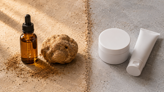 Amber bottle of Kamah truffle water with a whole desert truffle and sand beside plain unbranded modern cosmetic jar and tube