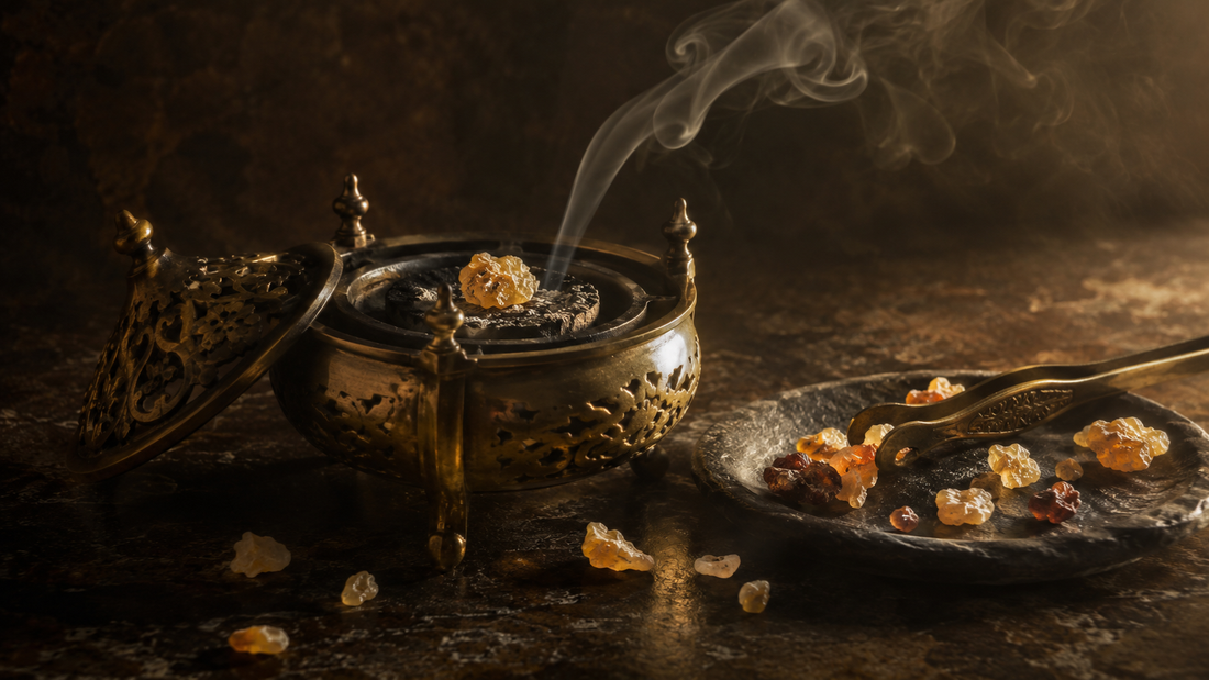 Brass incense burner with frankincense resin melting on charcoal and a thin ribbon of smoke, with metal tongs and scattered resin tears