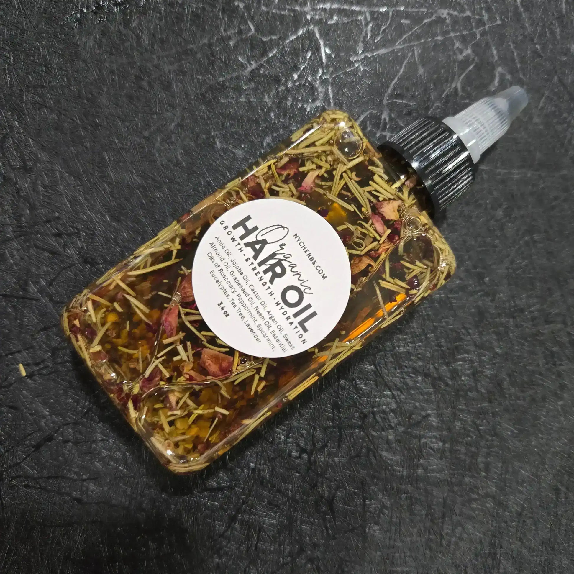 Organic herbal hair oil bottle with natural dried herbs on black textured background