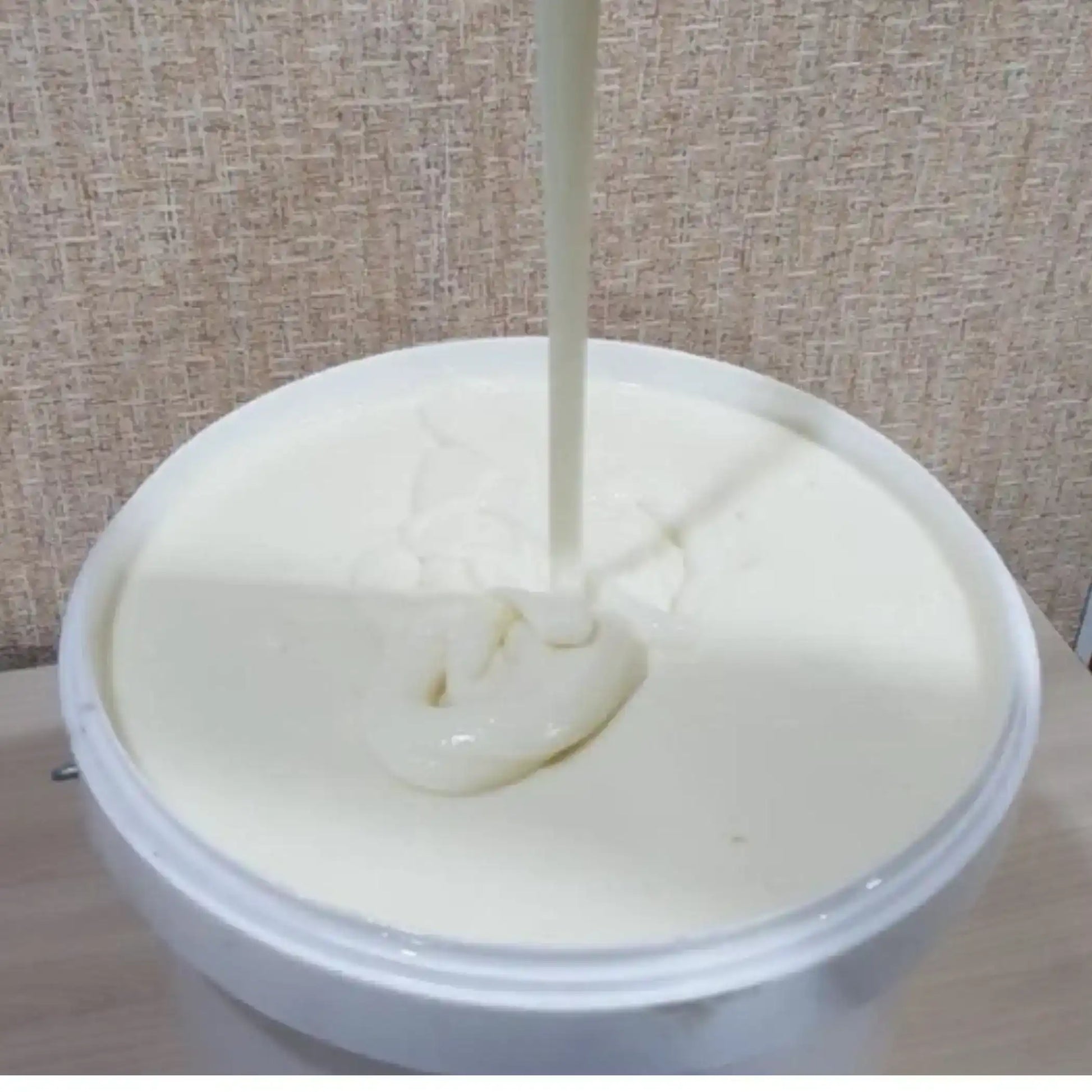 Creamy tahini paste being poured into a white tub, Middle Eastern food ingredient