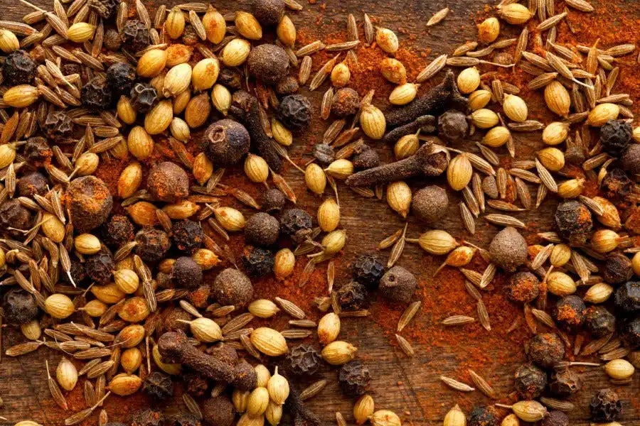 Assorted Middle Eastern spices including cumin, cloves, and peppercorns on a rustic wooden surface