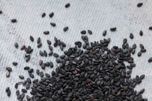 Black sesame seeds scattered on textured surface, natural Middle Eastern spice ingredient