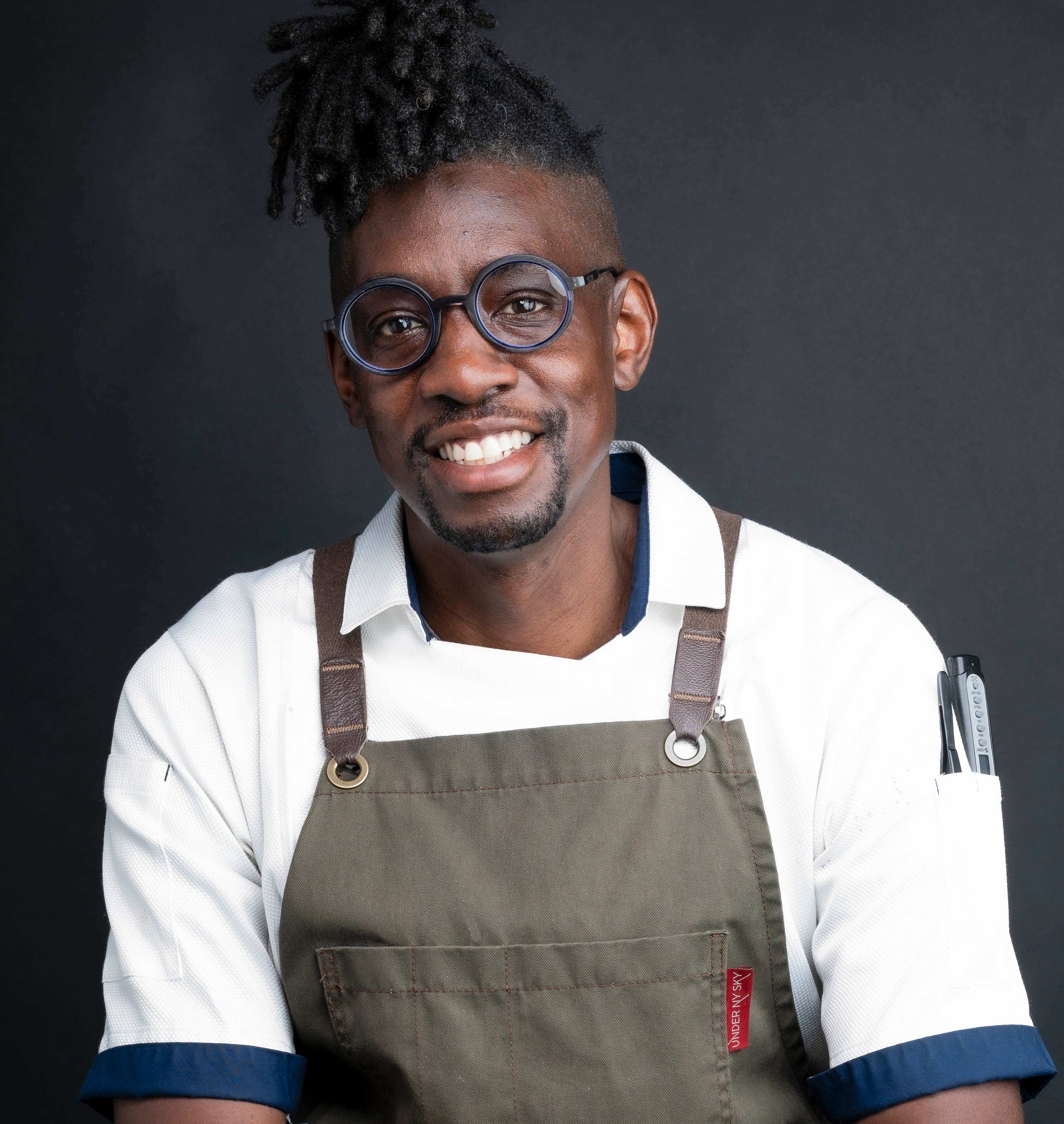 Chef wearing apron and glasses, smiling confidently in kitchen setting