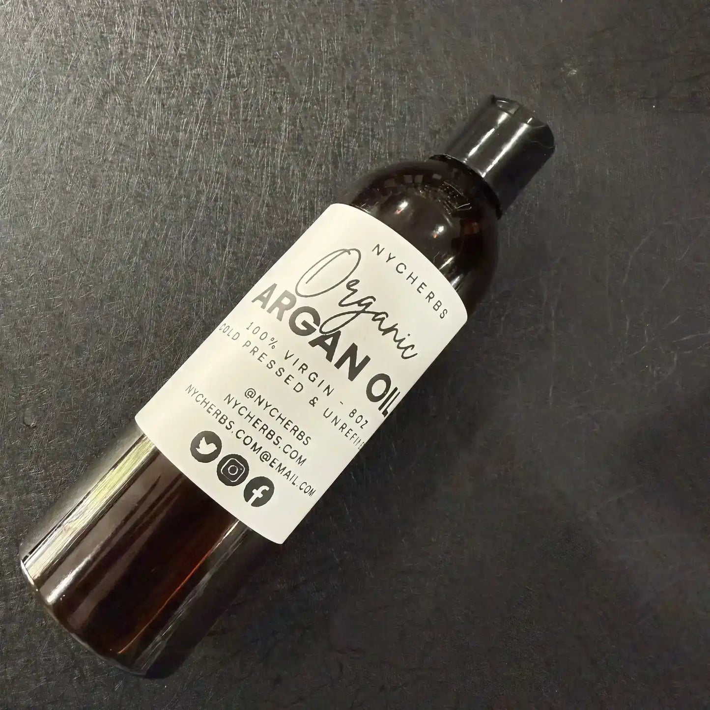 Bottle of organic cold-pressed argan oil on dark textured surface