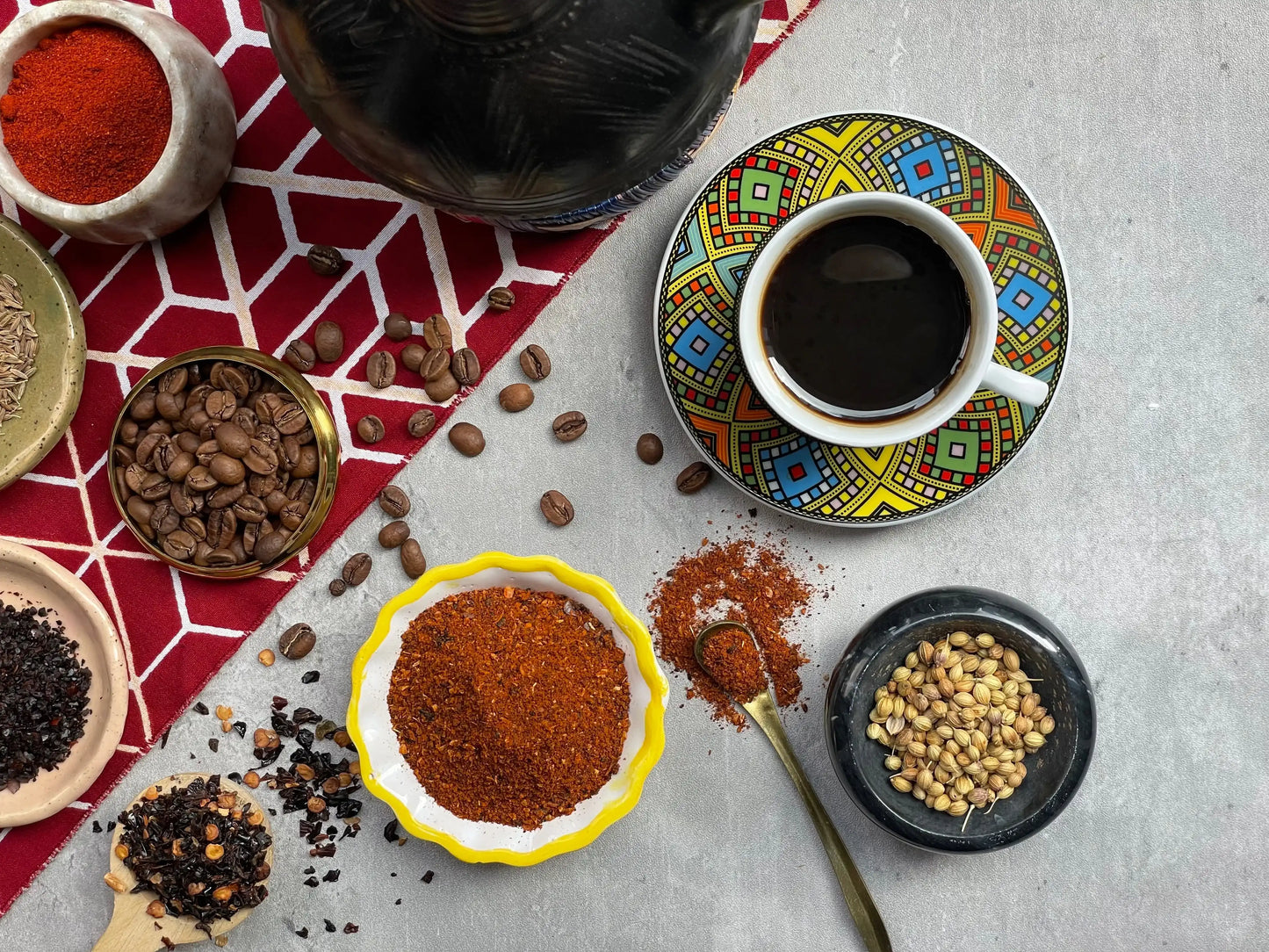 Middle Eastern spices, coffee beans, and herbs arranged with a cup of coffee on a colorful patterned saucer