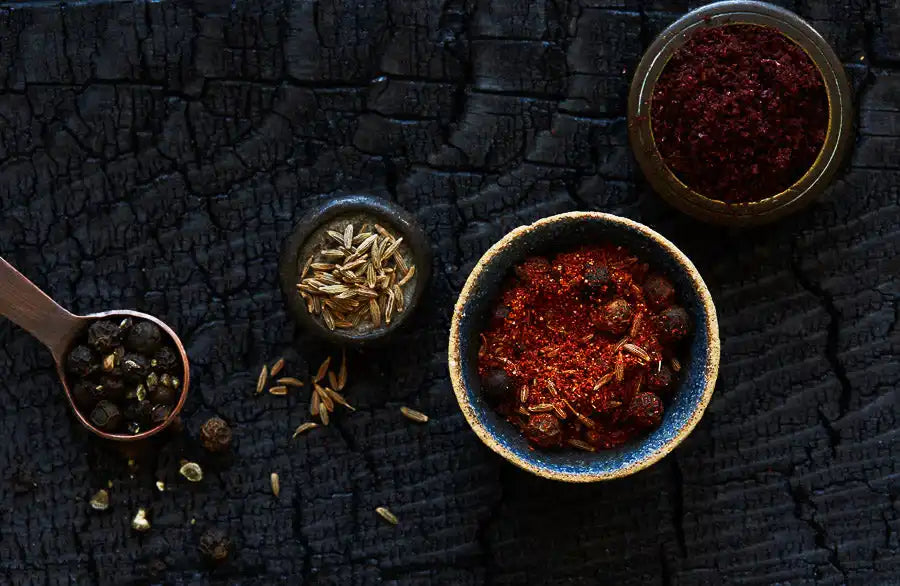 Assorted Middle Eastern spices including peppercorns, cumin, and paprika on a dark textured surface