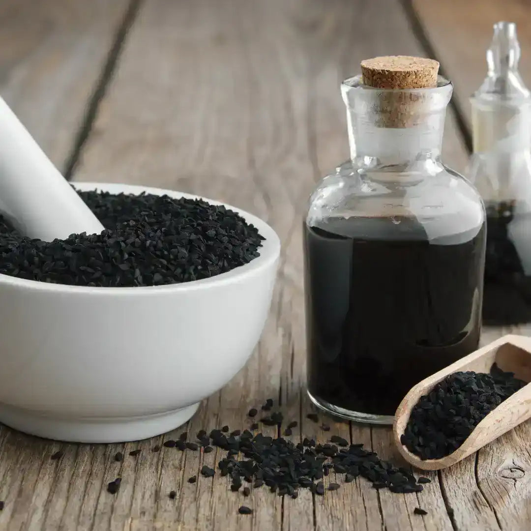 Black seed oil in glass bottle with whole black cumin seeds and mortar on wooden table