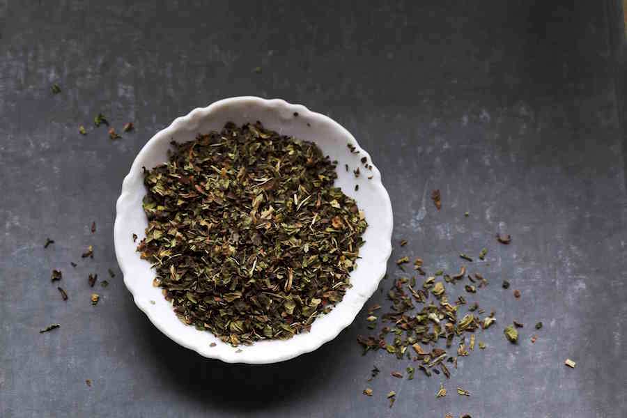 Dried Middle Eastern herbs in a white bowl, scattered on dark surface
